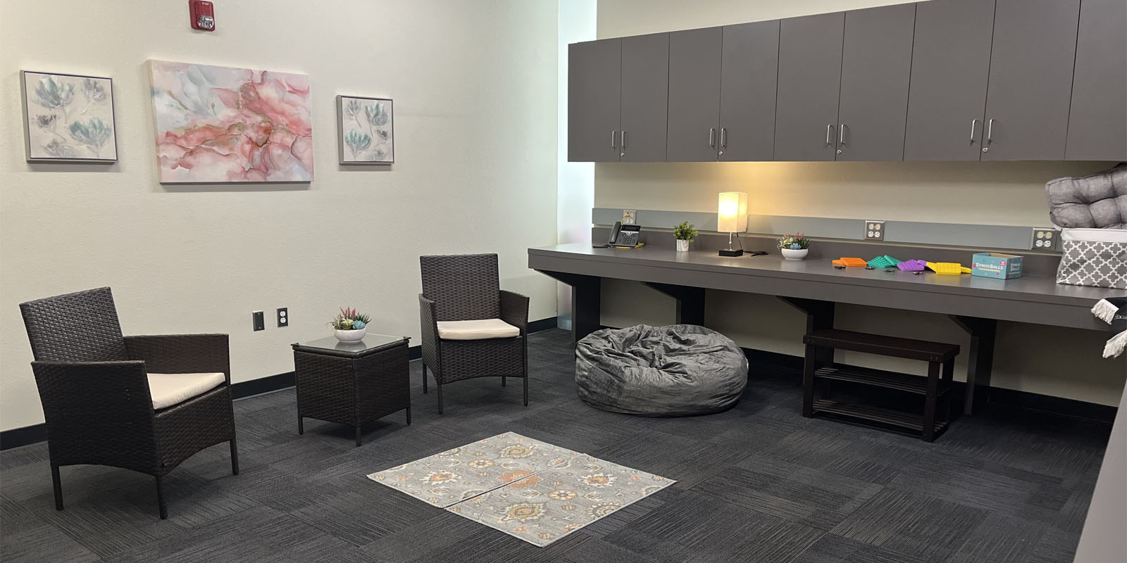 Reflection room with two chairs, a table, three pictures on the wall, two rugs, pillows, a bean bag chair, and electric candle