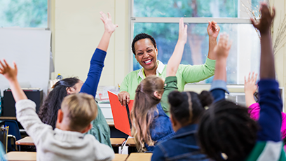 teacher facing classroom of students with raised hands 