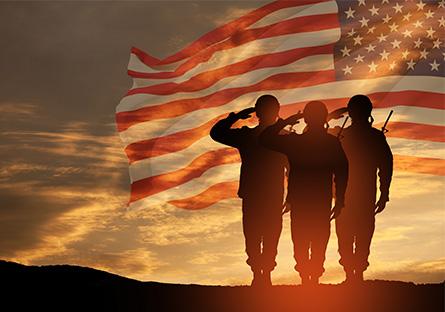 military personnel standing on a hill saluting with a flag superimposed over the sunset